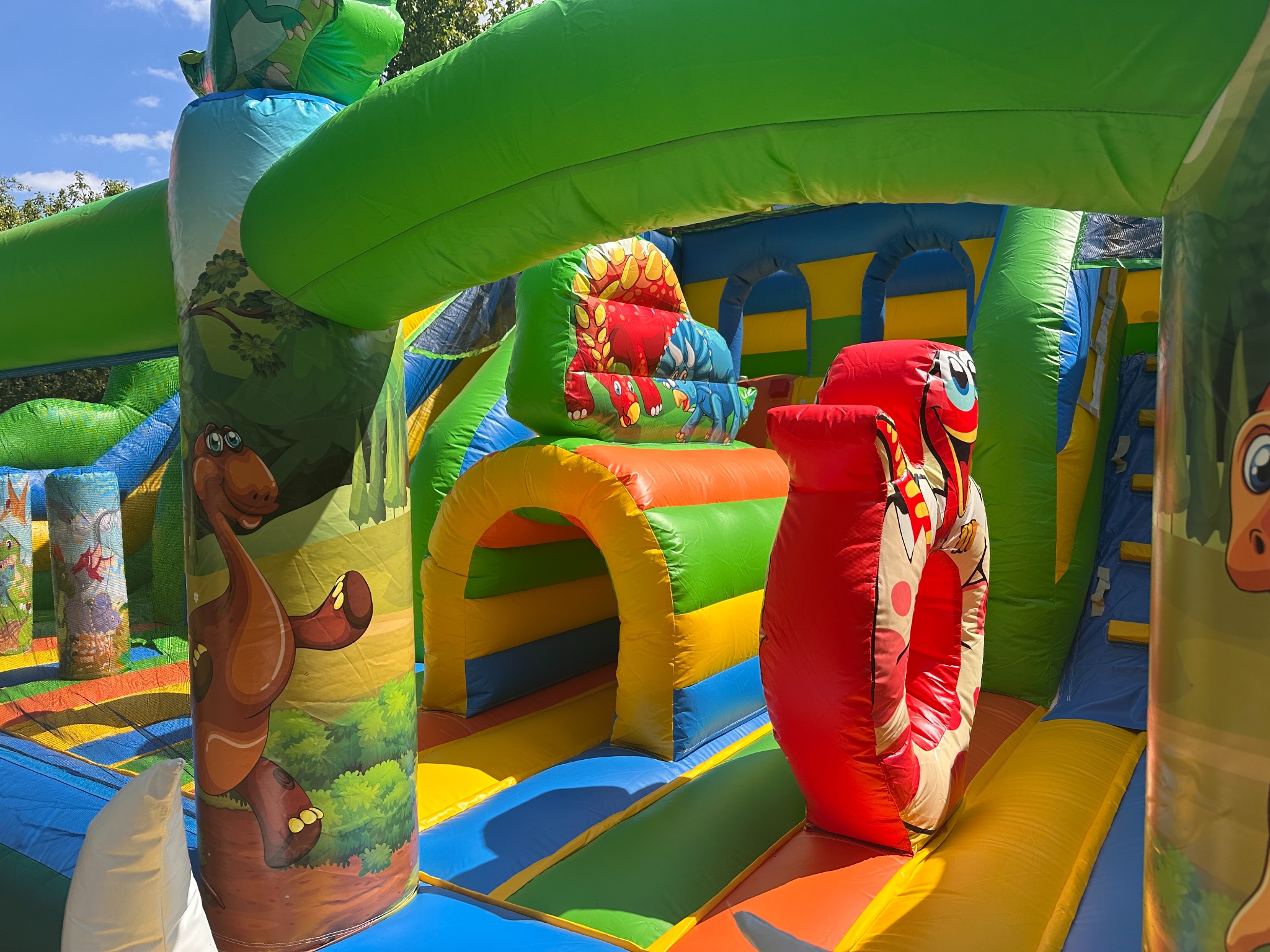 Kolorowy dmuchany zamek z motywem dinozaurów, atrakcja dla dzieci z tunelem, schodami i zjeżdżalnią, idealny na imprezy plenerowe.