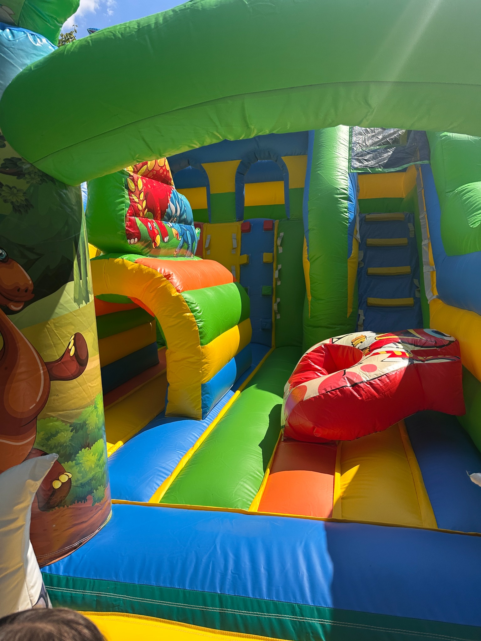 Kolorowy dmuchany zamek z motywami zwierzęcymi, widok od wewnątrz. Schody, zjeżdżalnia i tunel tworzą atrakcyjny plac zabaw dla dzieci.