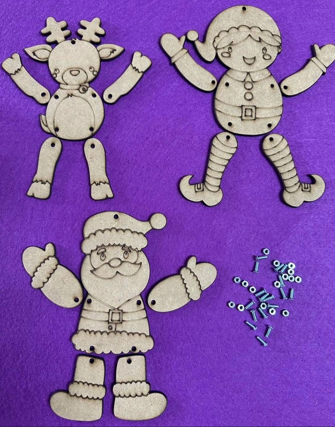 Drewniane, rozłożone figurki świąteczne (renifer, elf, Mikołaj) z ruchomymi elementami i zestawem śrubek na fioletowym tle. Kreatywny zestaw do samodzielnego montażu.