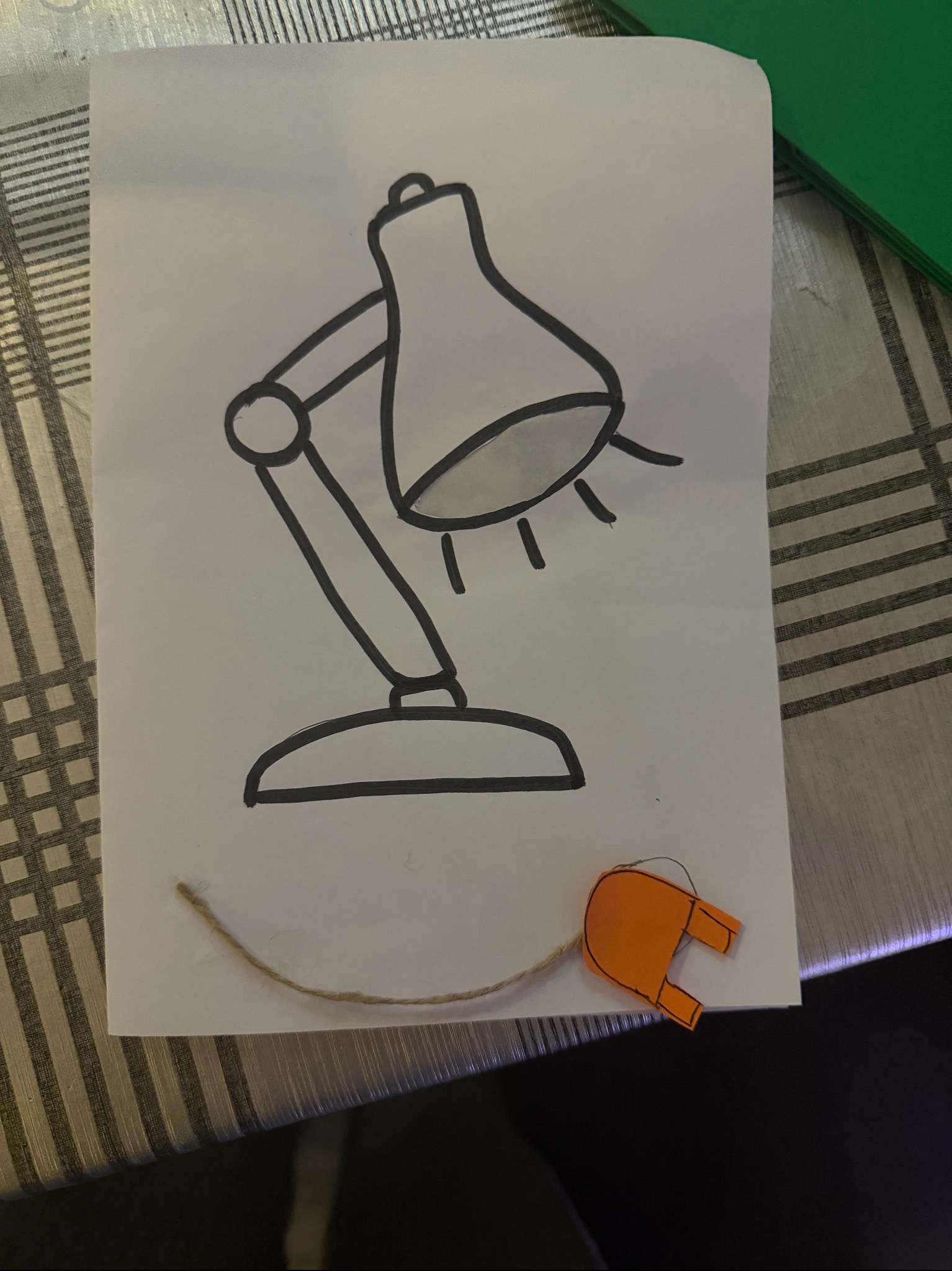 Ręcznie rysowana lampka biurkowa z pomarańczową wtyczką na kartce, leżąca na stole w Przyłęku. Kreatywna dekoracja na imprezę dla dzieci.