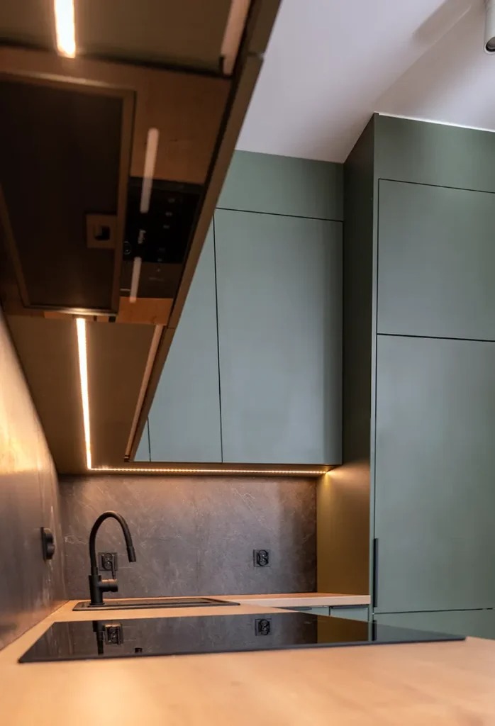 Nowoczesna kuchnia z zielonymi szafkami, czarnym zlewem i płytą indukcyjną. Oświetlenie LED podkreśla blat i przestrzeń roboczą. Minimalistyczny design.