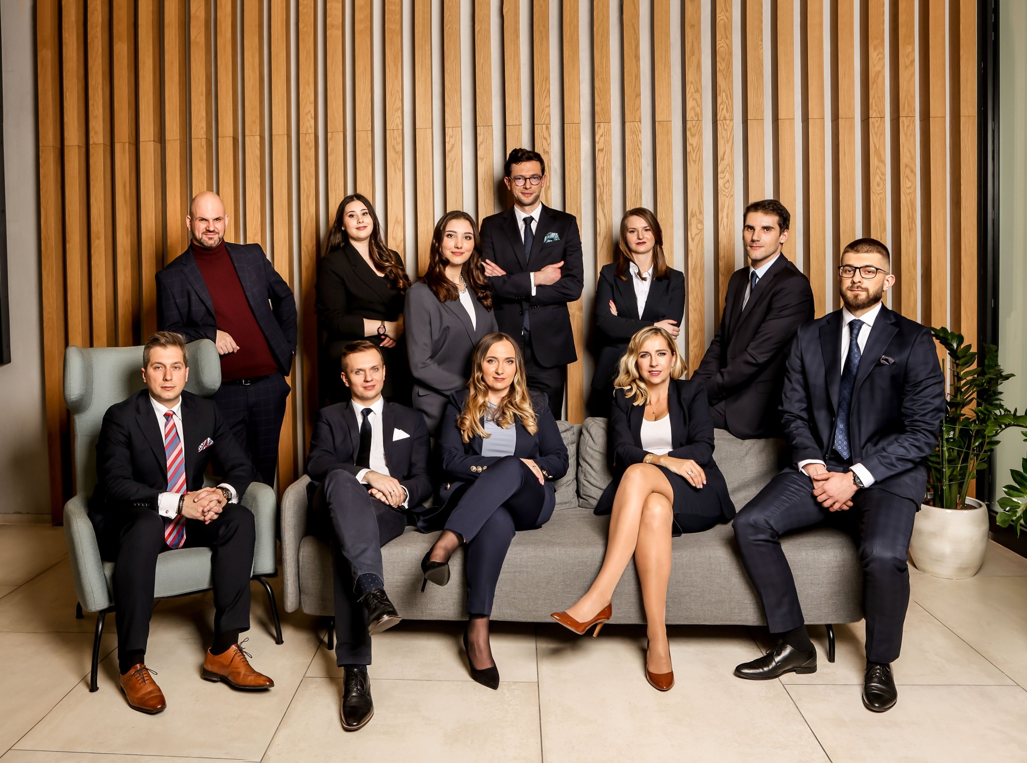Zgrany zespół prawników z Krakowa w eleganckich strojach pozuje na tle drewnianej ściany, tworząc profesjonalny wizerunek kancelarii.