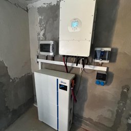 GROMAR-AUTO Mariusz Gromowski - Biały magazyn energii Deye z inwerterem i rozdzielnicami na surowej ścianie. Widoczne kable i elementy instalacji. Montaż w trakcie wykończenia.