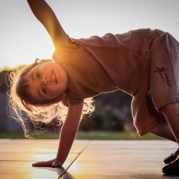 Patryk Fijołek - Uśmiechnięta dziewczynka robi mostek na tle zachodzącego słońca, na jej ubraniu widnieje napis SUMMER i palma.