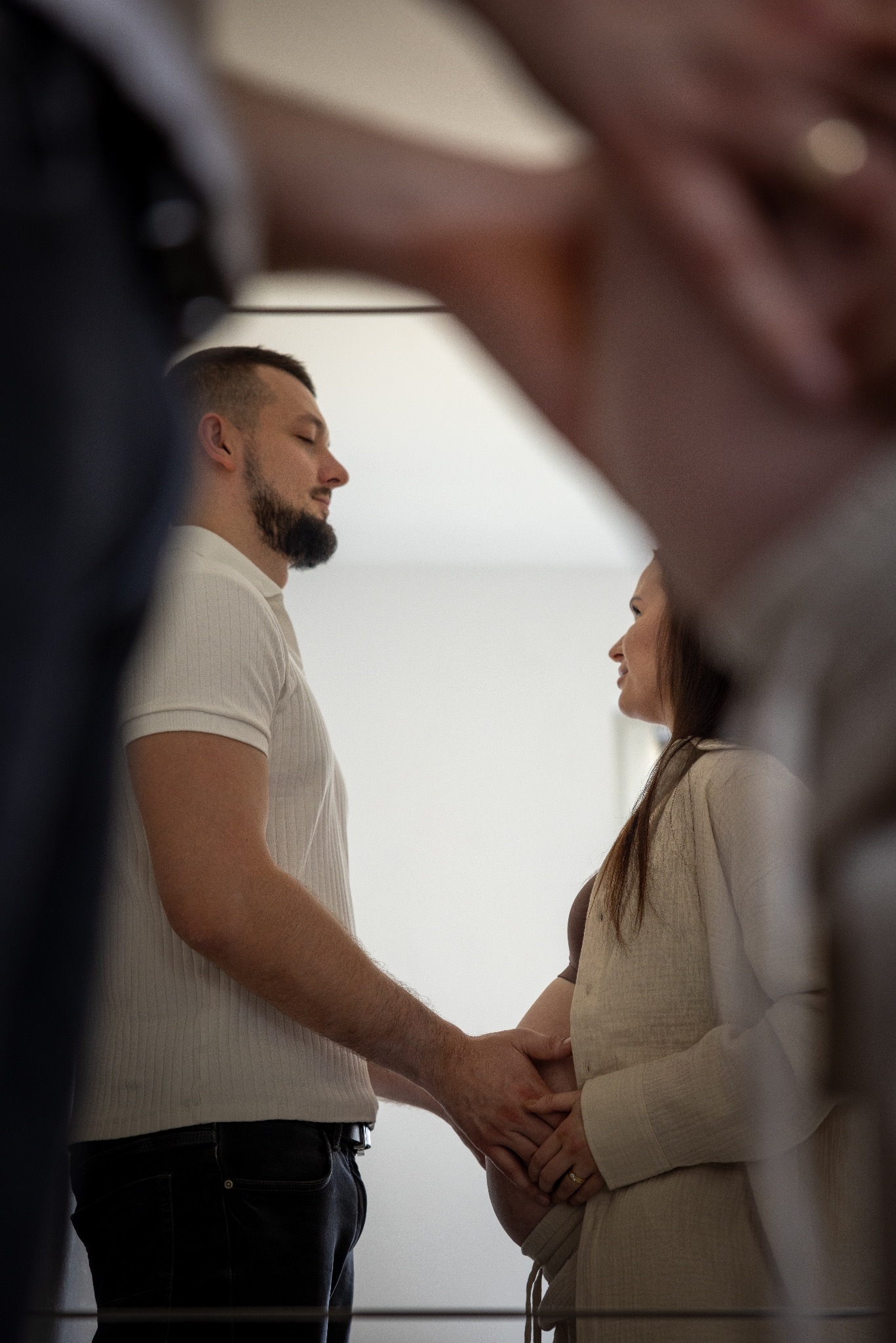 Czułe ujęcie: przyszły tata obejmuje dłońmi ciążowy brzuszek partnerki, oboje patrzą na siebie z miłością, kadr z unikalnej perspektywy.