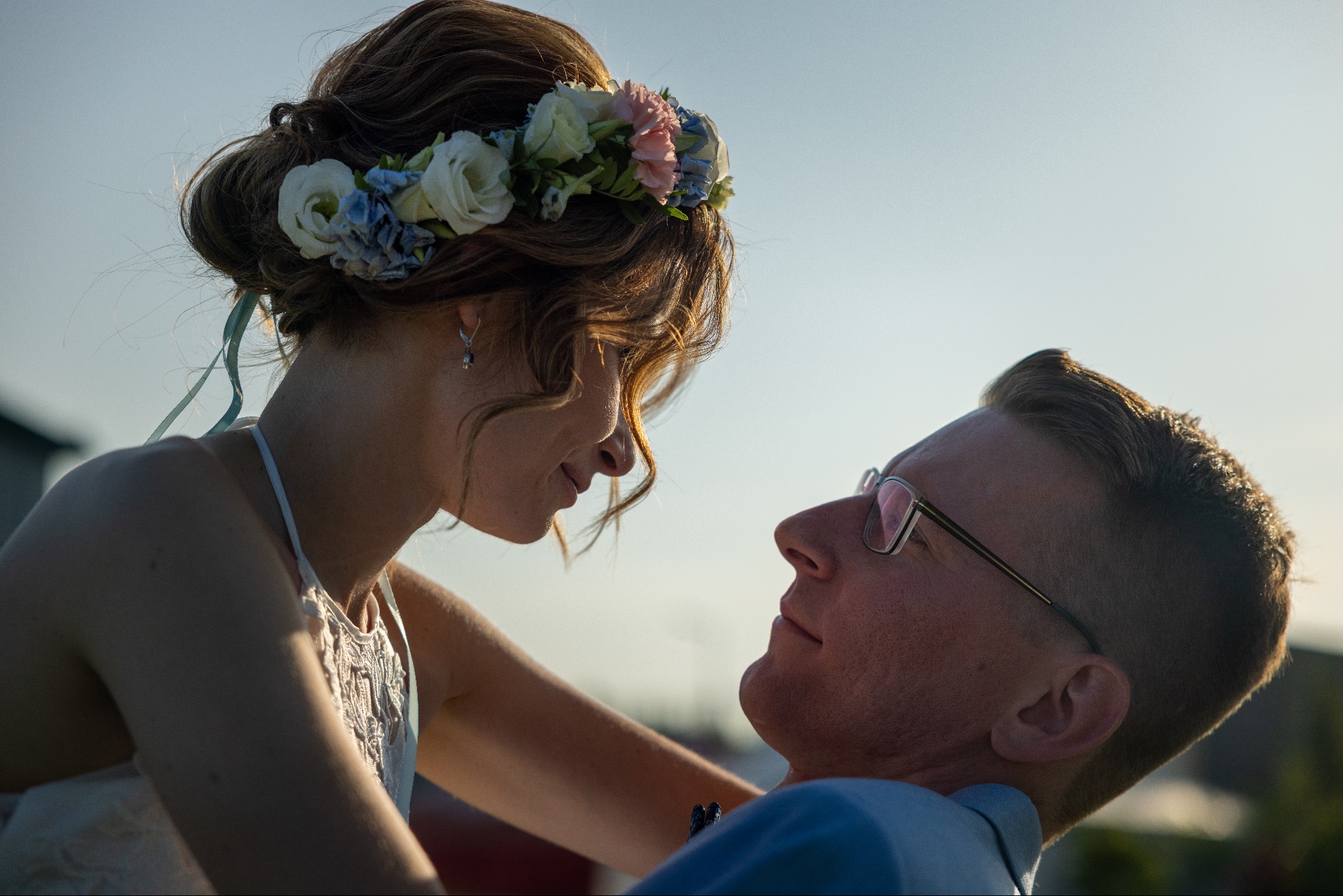 Zakochana para w zbliżeniu: panna młoda z wiankiem i pan młody w okularach patrzą na siebie w słoneczny dzień. Romantyczny moment.