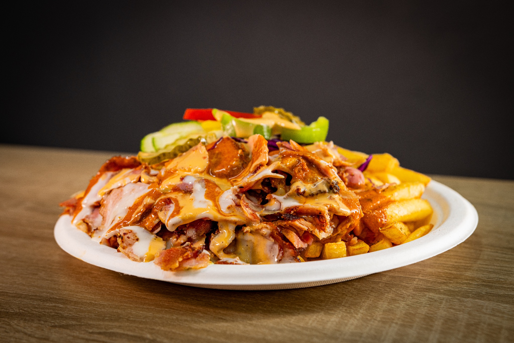 Apetyczny kebab na talerzu z frytkami i sosem, na drewnianym stole i ciemnym tle. Widoczne kolorowe warzywa. Zdjęcie z bliska, podkreślające świeżość składników.