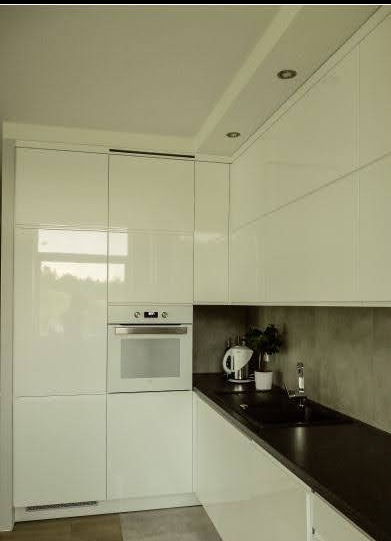 Elegancka kuchnia w białym połysku, z piekarnikiem w słupku i czarnym blatem.