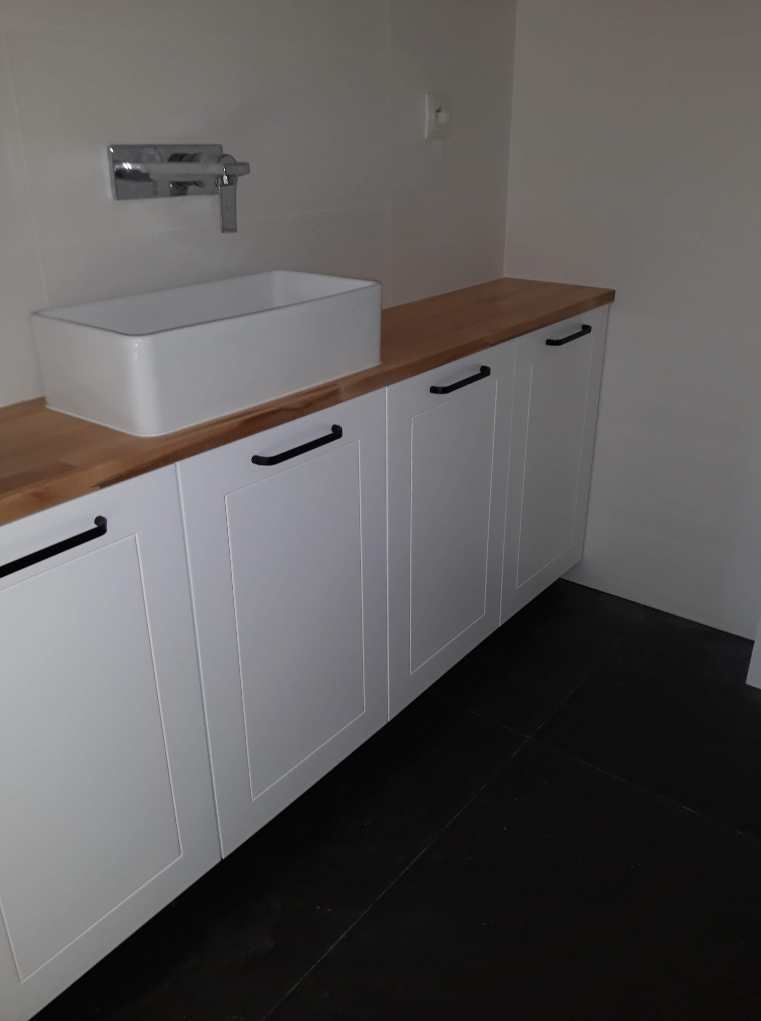 Łazienka – biała szafka z umywalką nablatową, drewniany blat, ciemna podłoga.