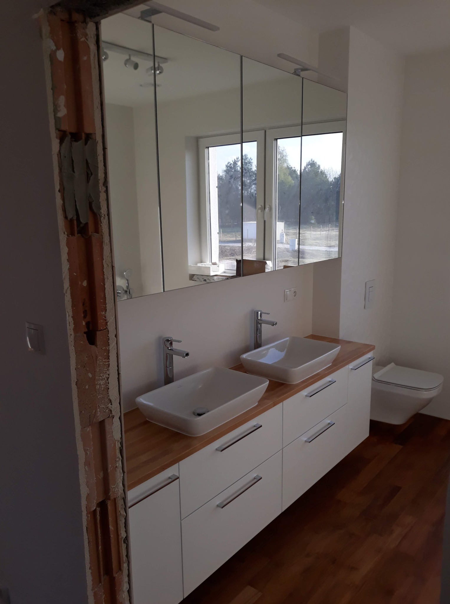 Nowoczesna szafka łazienkowa z dwiema umywalkami nablatowymi i lustrem w zabudowie. Widoczny fragment ściany w trakcie prac wykończeniowych.