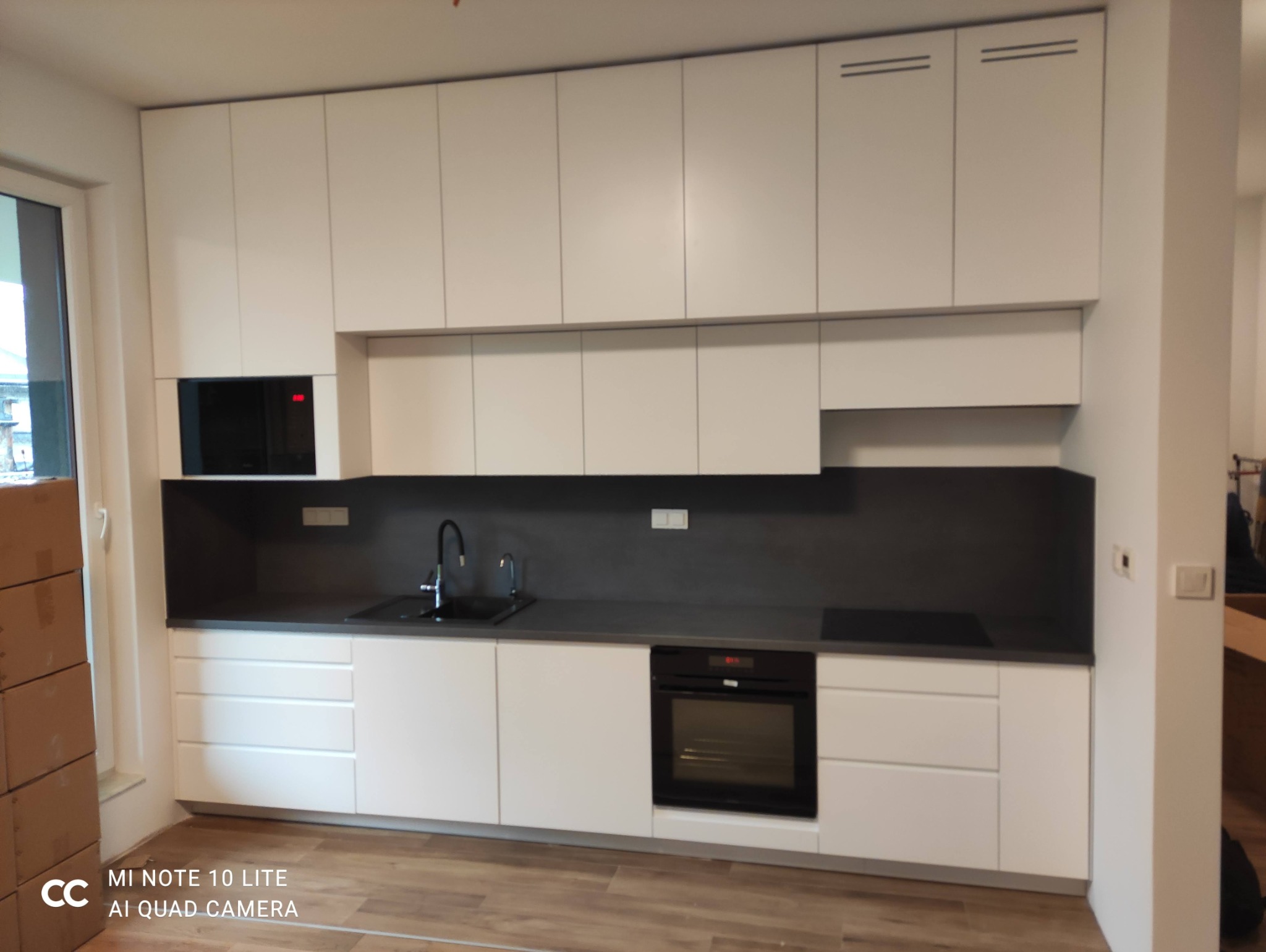 Nowoczesna kuchnia w zabudowie – fronty jasne, blat i panel w kolorze grafitowym, sprzęty w zabudowie.