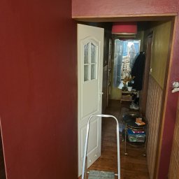 Marcin Brzeski - Ściana w odcieniach czerwieni po odświeżeniu, widoczna drabina malarska i otwarte drzwi do przedpokoju. Prace wykończeniowe w trakcie realizacji.