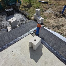 KAMIL TARGONI USŁUGI OGÓLNOBUDOWLANE I STOLARSKIE - Budowa fundamentów: bloczki silikatowe z otworami na papie dachowej Lemar, przygotowane do dalszych prac murarskich. Widoczne zbrojenie i materiały izolacyjne.