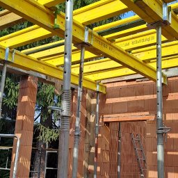 KAMIL TARGONI USŁUGI OGÓLNOBUDOWLANE I STOLARSKIE - Wznoszenie murów z pustaków ceramicznych. Żółte, drewniane stemple podtrzymują strop. Widoczne drabiny i elementy szalunków stropowych.