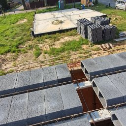 KAMIL TARGONI USŁUGI OGÓLNOBUDOWLANE I STOLARSKIE - Budowa domu: Widok z góry na strop Teriva z szarych bloczków, w tle fundamenty, teren budowy i zabudowa jednorodzinna w słoneczny dzień.