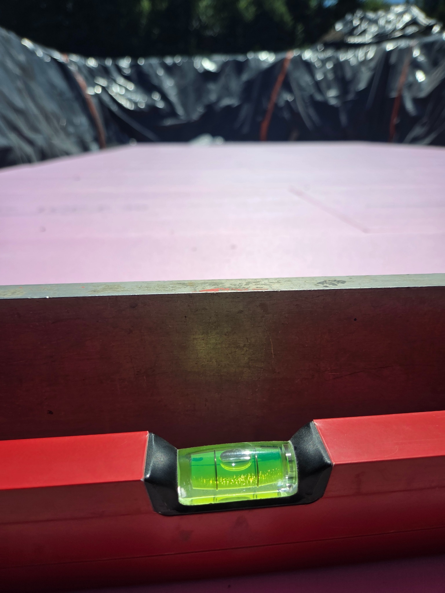 Poziomica na różowej izolacji fundamentu, czarna folia w tle. Sprawdzanie poziomu izolacji przed wylaniem fundamentu.