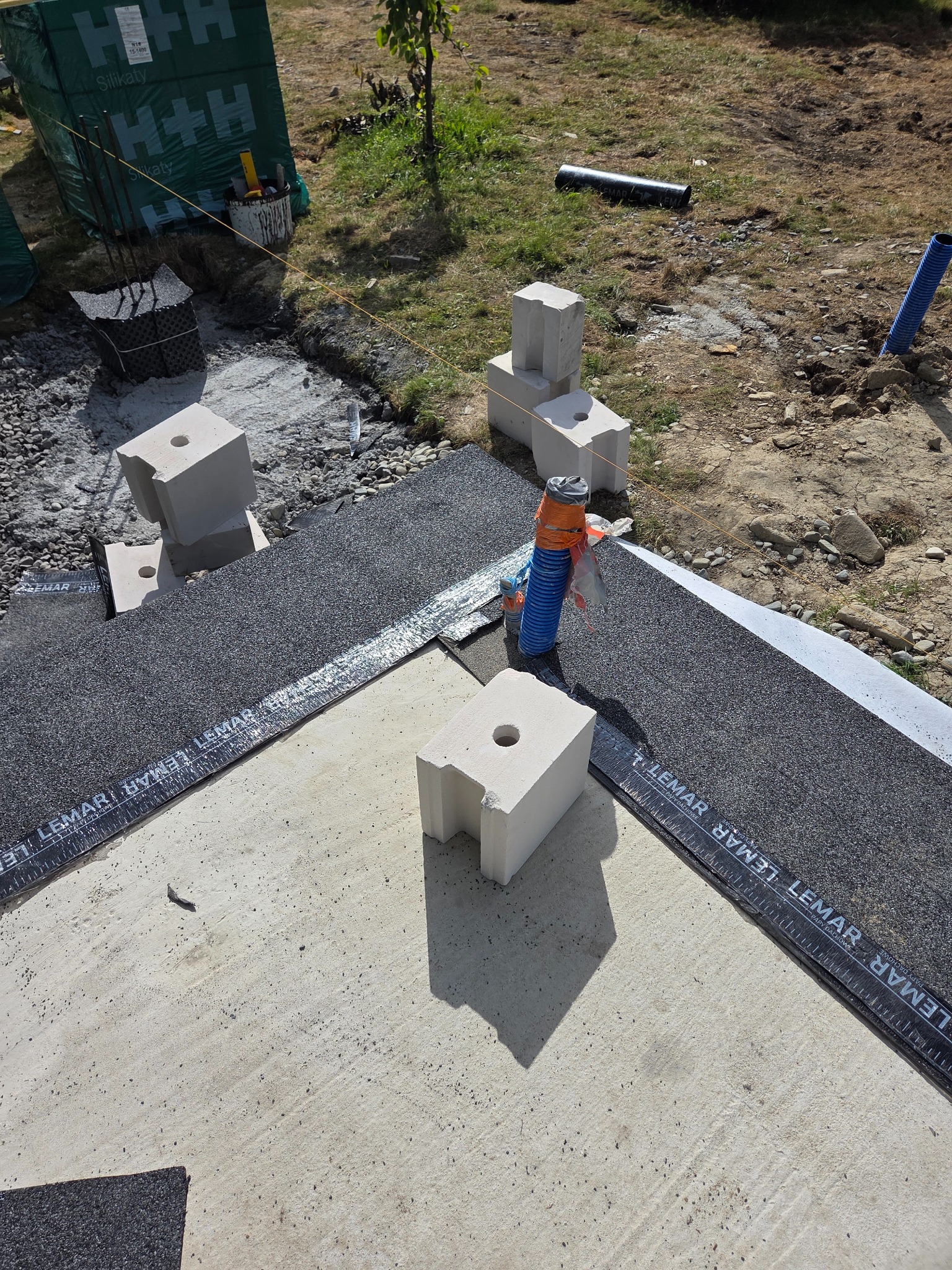 Budowa fundamentów: bloczki silikatowe z otworami na papie dachowej Lemar, przygotowane do dalszych prac murarskich. Widoczne zbrojenie i materiały izolacyjne.