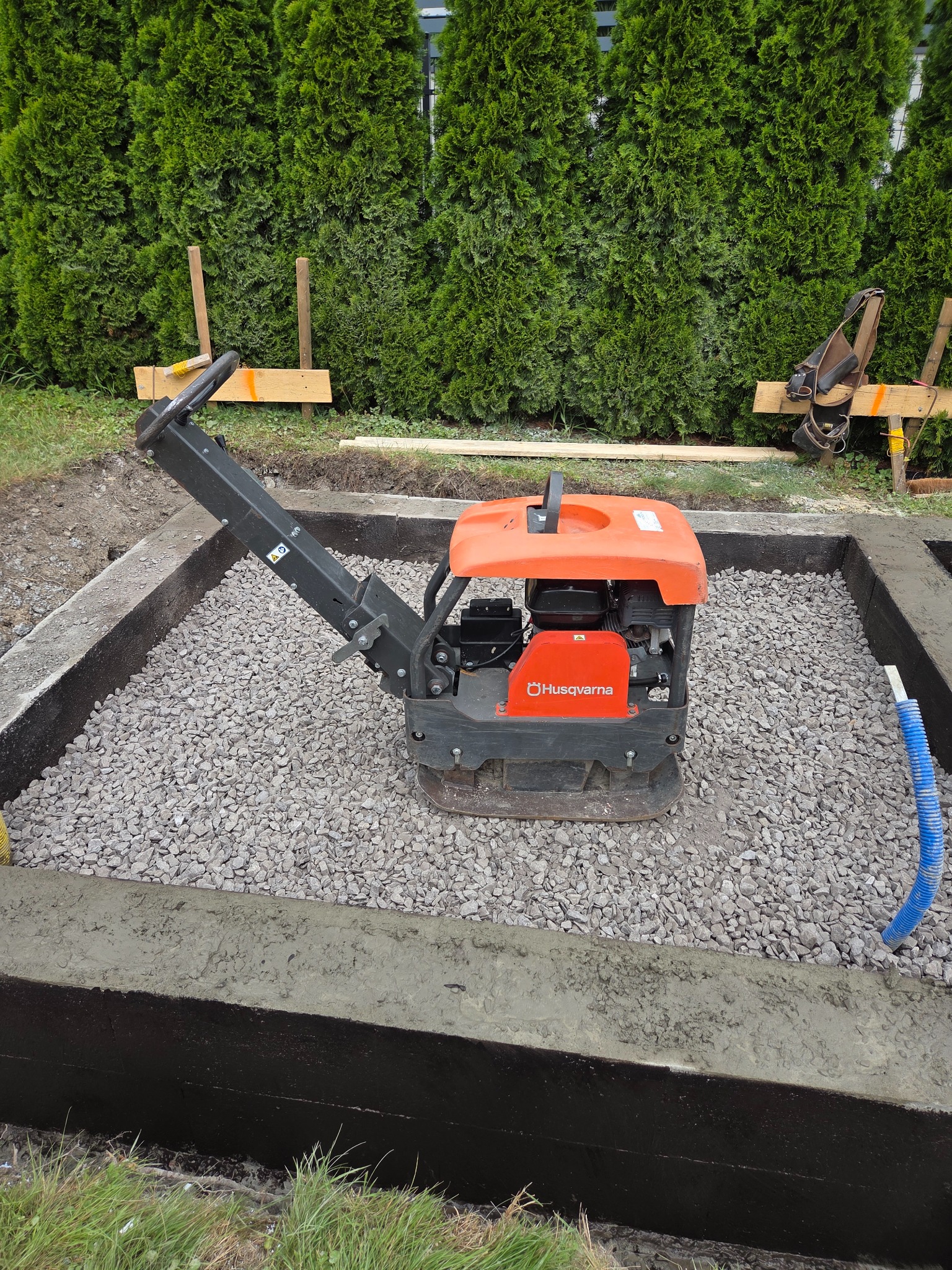 Zagęszczarka Husqvarna ubija żwir w fundamencie w Pszczynie. Izolacja pionowa fundamentu z naniesioną warstwą hydroizolacyjną. Widoczne szalunki.