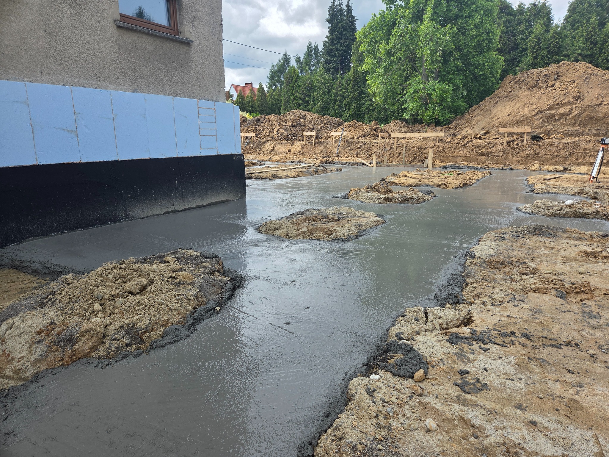 Wylany fundament pod budynek z izolacją termiczną. Widoczne szalunki i ziemia. Świeży beton tworzy gładką powierzchnię.