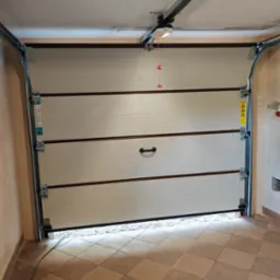 Otwarta segmentowa brama garażowa w kolorze kremowym, z widocznym mechanizmem automatycznym na suficie garażu i częściowo widocznymi płytkami podłogowymi.