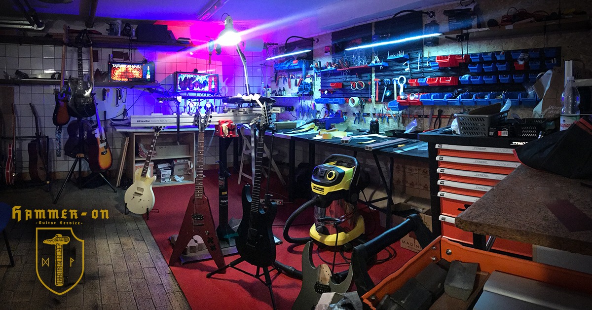 Warsztat naprawy gitar z narzędziami i instrumentami. Uwagę przykuwa żółty odkurzacz Karcher oraz logotyp firmy 'Hammer-On Guitar Service'.