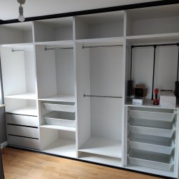 Michał Kamiński - Biała szafa wnękowa z czarnymi akcentami, otwarte półki, drążki na ubrania i wysuwane kosze. Na podłodze narzędzia montażowe.