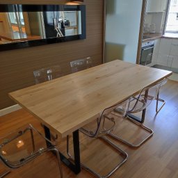 Michał Kamiński - Drewniany stół jadalny z czarnymi nogami i przezroczystymi krzesłami w nowoczesnym wnętrzu z lustrem i oświetleniem.