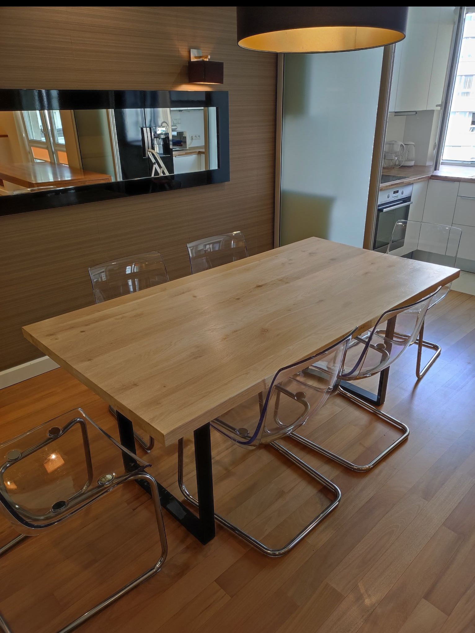 Drewniany stół jadalny z czarnymi nogami i przezroczystymi krzesłami w nowoczesnym wnętrzu z lustrem i oświetleniem.