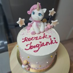 Pan Pierożek - Tort jednorożec na roczek Jagienki. Biały tort z różowymi akcentami, dekorowany figurką jednorożca i gwiazdkami. Napis wykonany różową polewą.