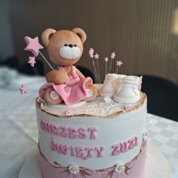 Pan Pierożek - Tort na chrzest z misiem w różowej sukience, małymi bucikami i napisem 'Chrzest Święty Zuzi'. Dekoracje z gwiazdek i kwiatów. Pastelowa kolorystyka.