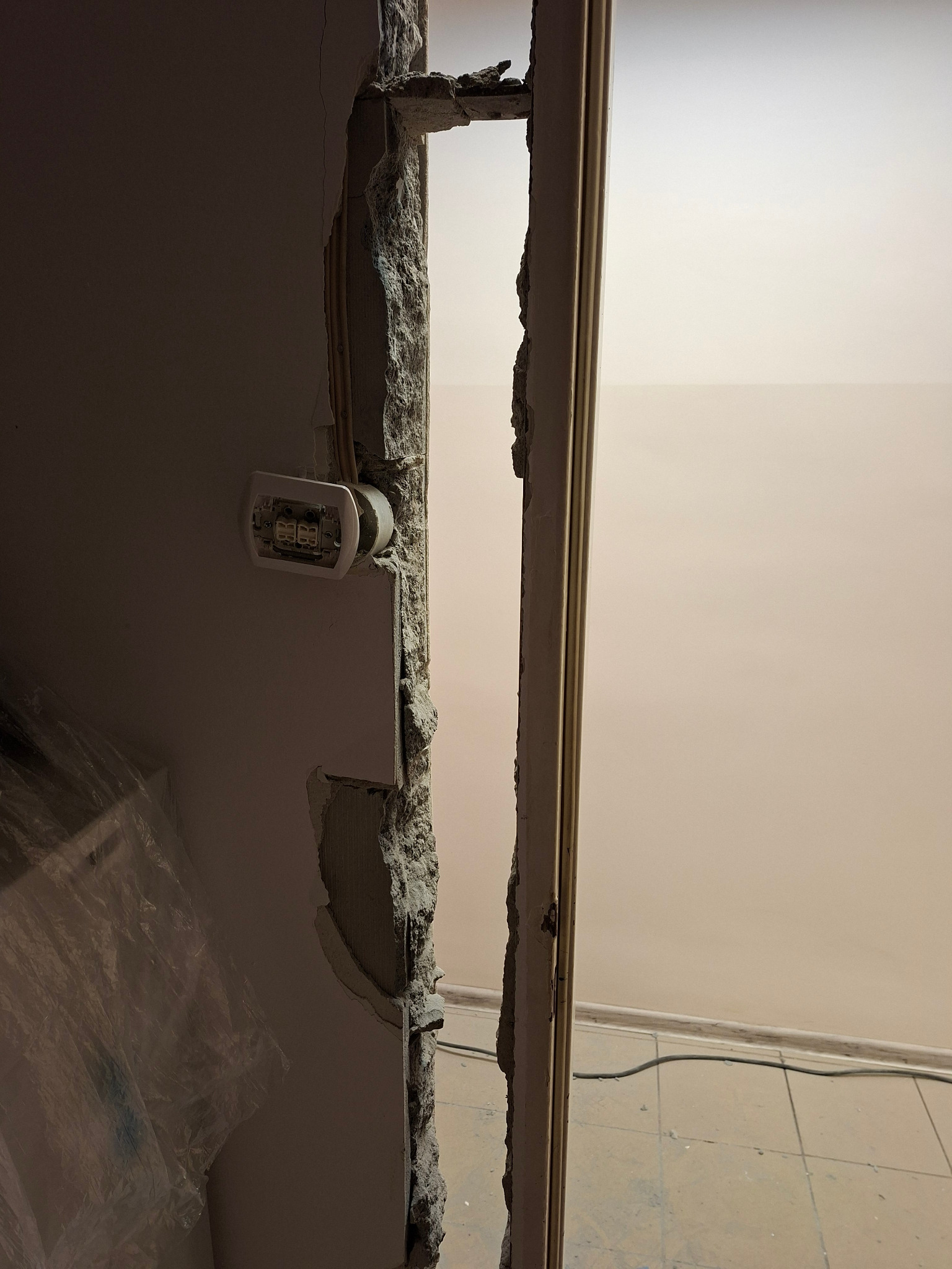 Fragment ściany po wyburzeniu z widoczną puszką elektryczną i resztkami futryny. Widoczne uszkodzenia i gruz.