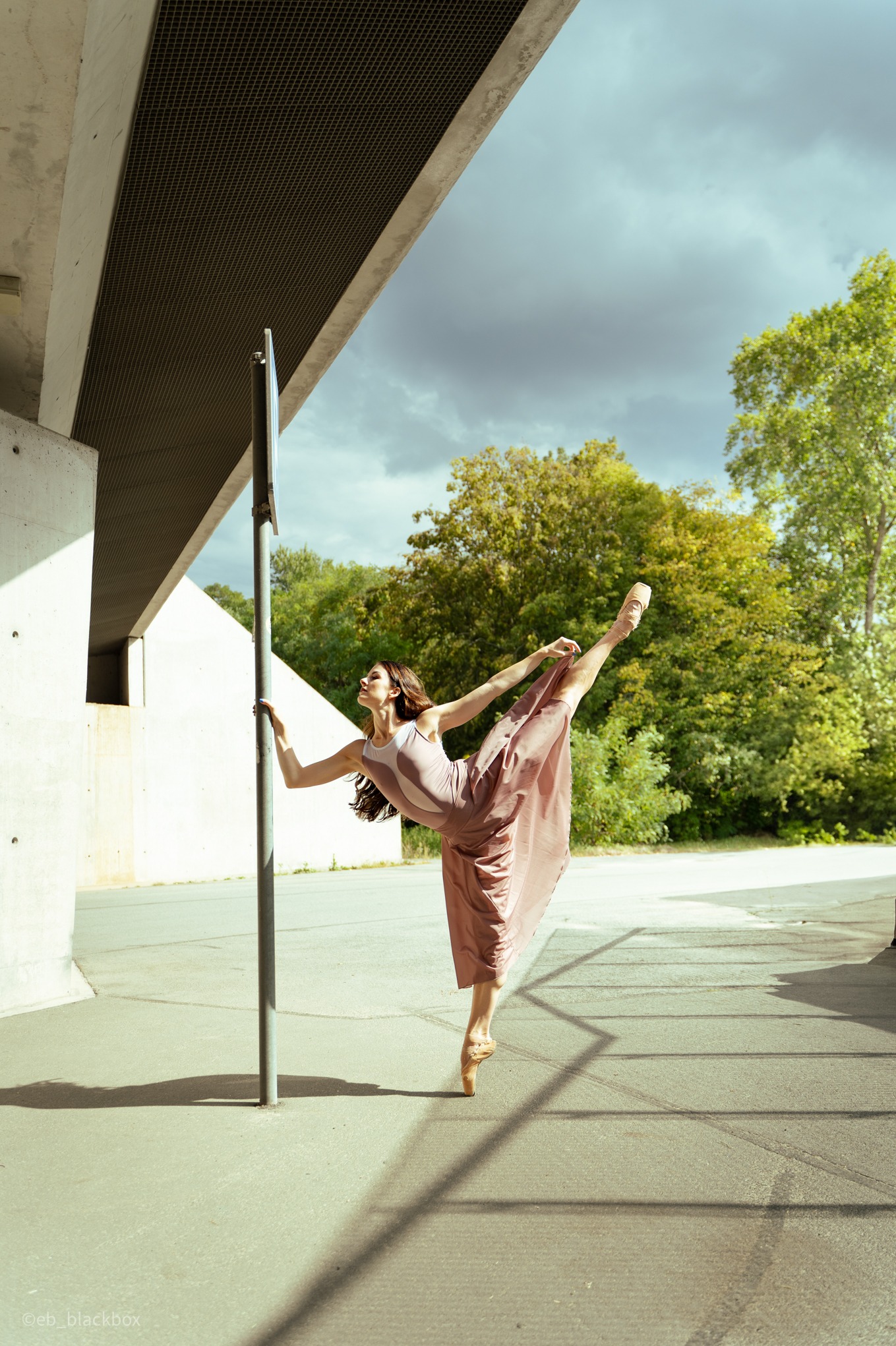 Baletnica w różowej sukience wykonuje figurę na tle betonowej architektury w słonecznym Wrocławiu. Dynamiczne ujęcie, taniec w przestrzeni miejskiej.