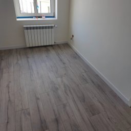 USŁUGI REMONTOWE MIKOŁAJ KARBOWIAK - Jasne panele podłogowe imitujące drewno w pokoju po remoncie. Białe ściany i grzejnik. Usługi wykończeniowe w Barcinie.