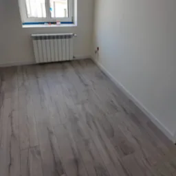 Jasne panele podłogowe imitujące drewno w pokoju po remoncie. Białe ściany i grzejnik. Usługi wykończeniowe w Barcinie.