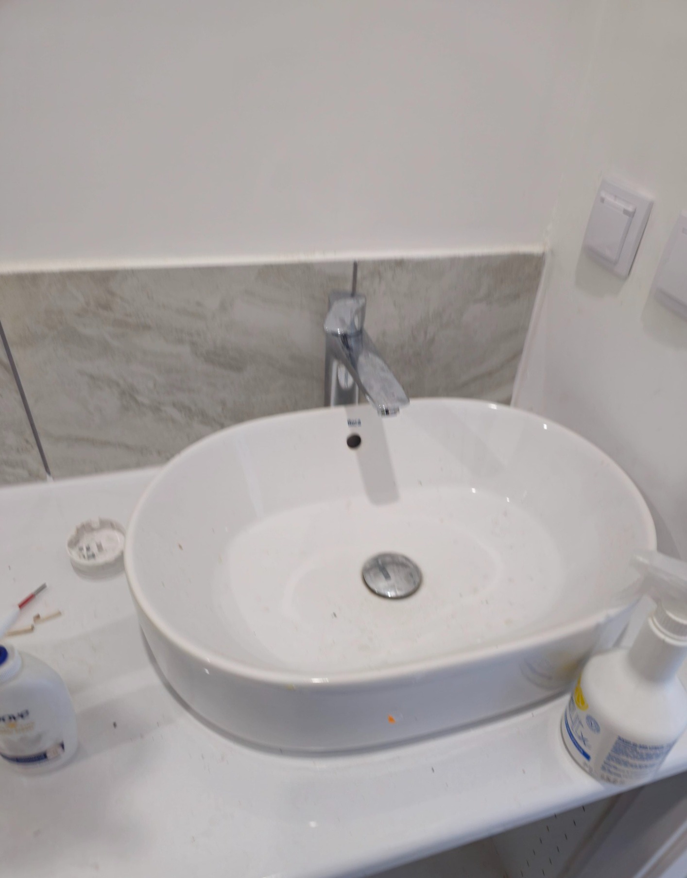 Biała umywalka z chromowaną baterią w trakcie montażu, widoczne narzędzia i akcesoria. Ujęcie z bliska, ukazujące detale instalacji w łazience.