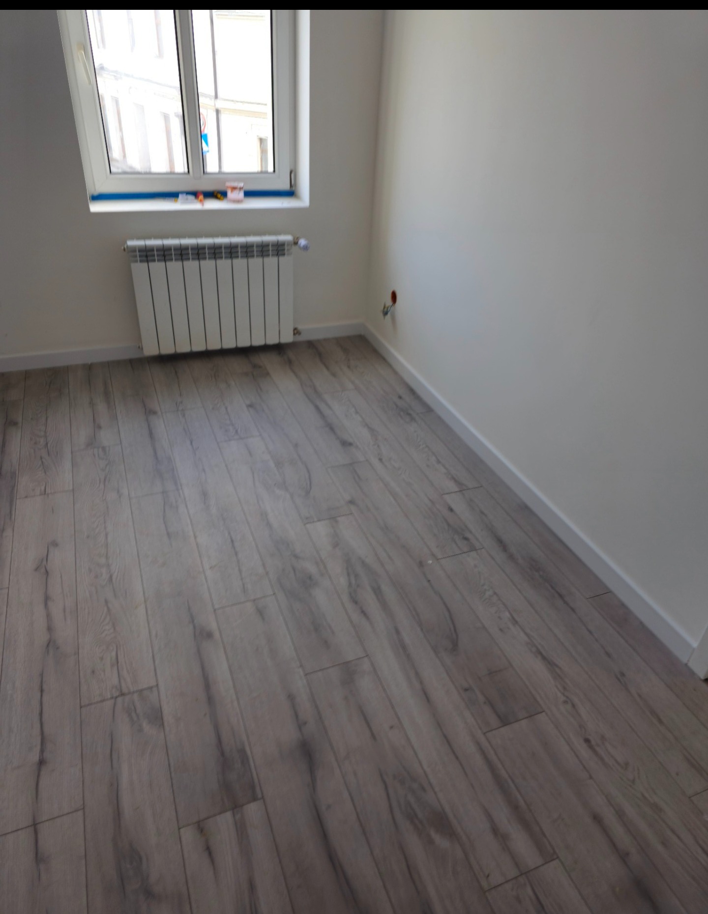 Jasne panele podłogowe imitujące drewno w pokoju po remoncie. Białe ściany i grzejnik. Usługi wykończeniowe w Barcinie.