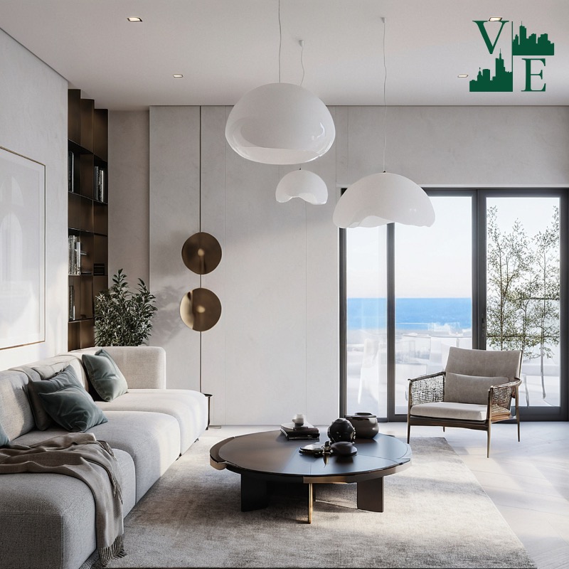 Jasne wnętrze salonu z widokiem na morze. Minimalistyczny design z sofą, stolikiem kawowym i designerskimi lampami. Duże okna wpuszczają naturalne światło.