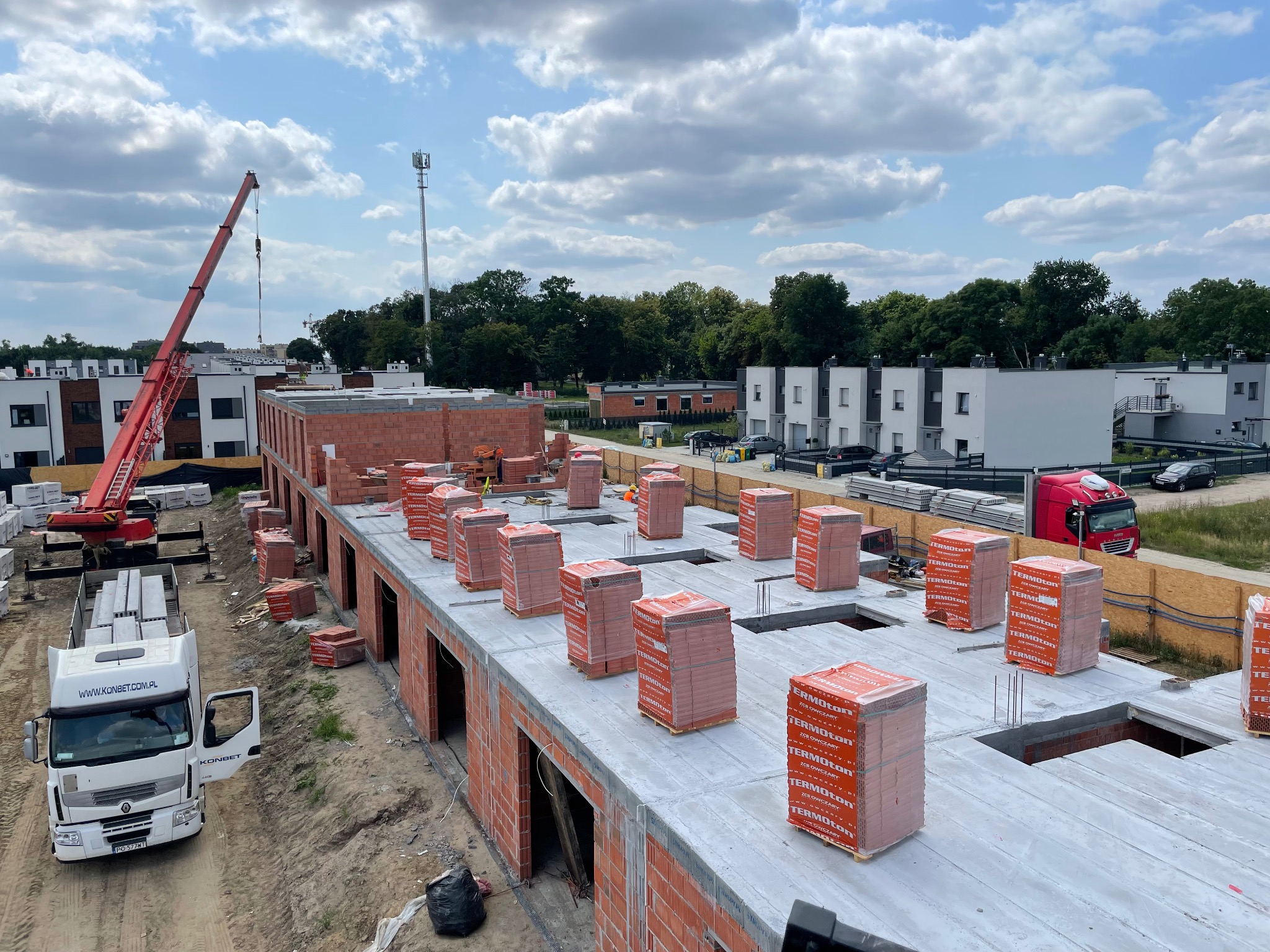 Budowa domu: widok z góry na strop z pustakami ceramicznymi Termoton. Na budowie dźwig i ciężarówka Konbet. W tle zabudowa osiedlowa i zieleń.