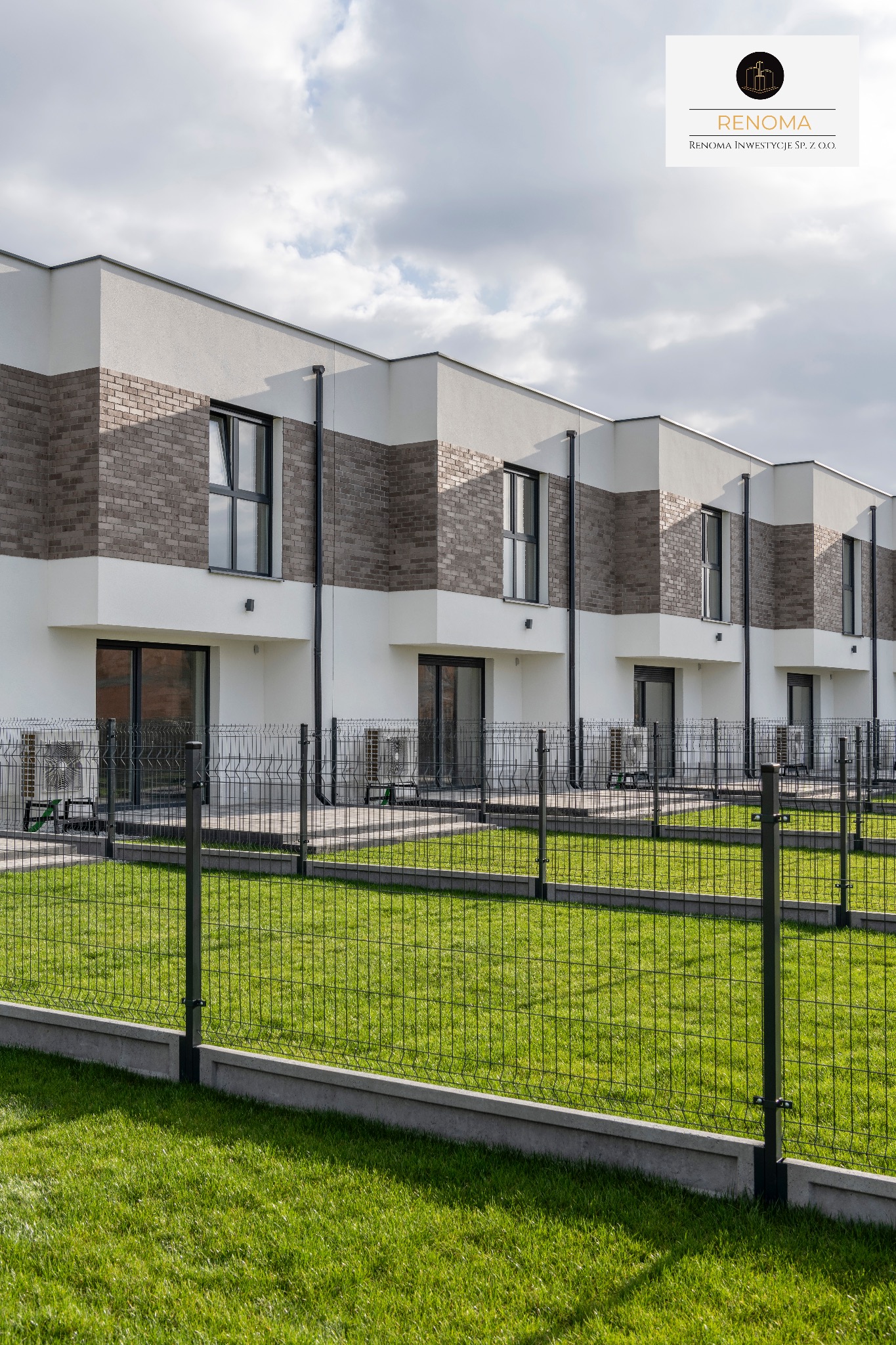 Szereg nowoczesnych domów z brązową cegłą i białym tynkiem, ogrodzonych siatką na tle zielonego trawnika i pochmurnego nieba. Widoczne klimatyzatory.
