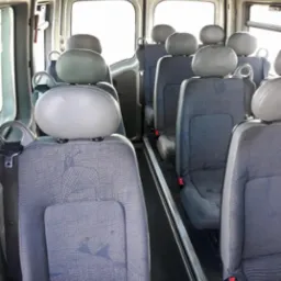 Wnętrze busa z rzędami szarych foteli z zagłówkami, widok z tyłu pojazdu w kierunku jasnych drzwi.