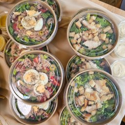 À la main party box & catering - Zestaw cateringowy: sałatki Cezar z grzankami i tuńczyk z jajkiem w ekologicznych opakowaniach z sosami, gotowe do serwowania na firmowym evencie.