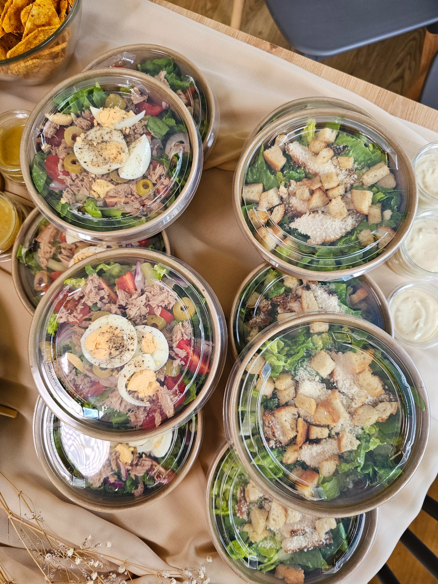 Zestaw cateringowy: sałatki Cezar z grzankami i tuńczyk z jajkiem w ekologicznych opakowaniach z sosami, gotowe do serwowania na firmowym evencie.