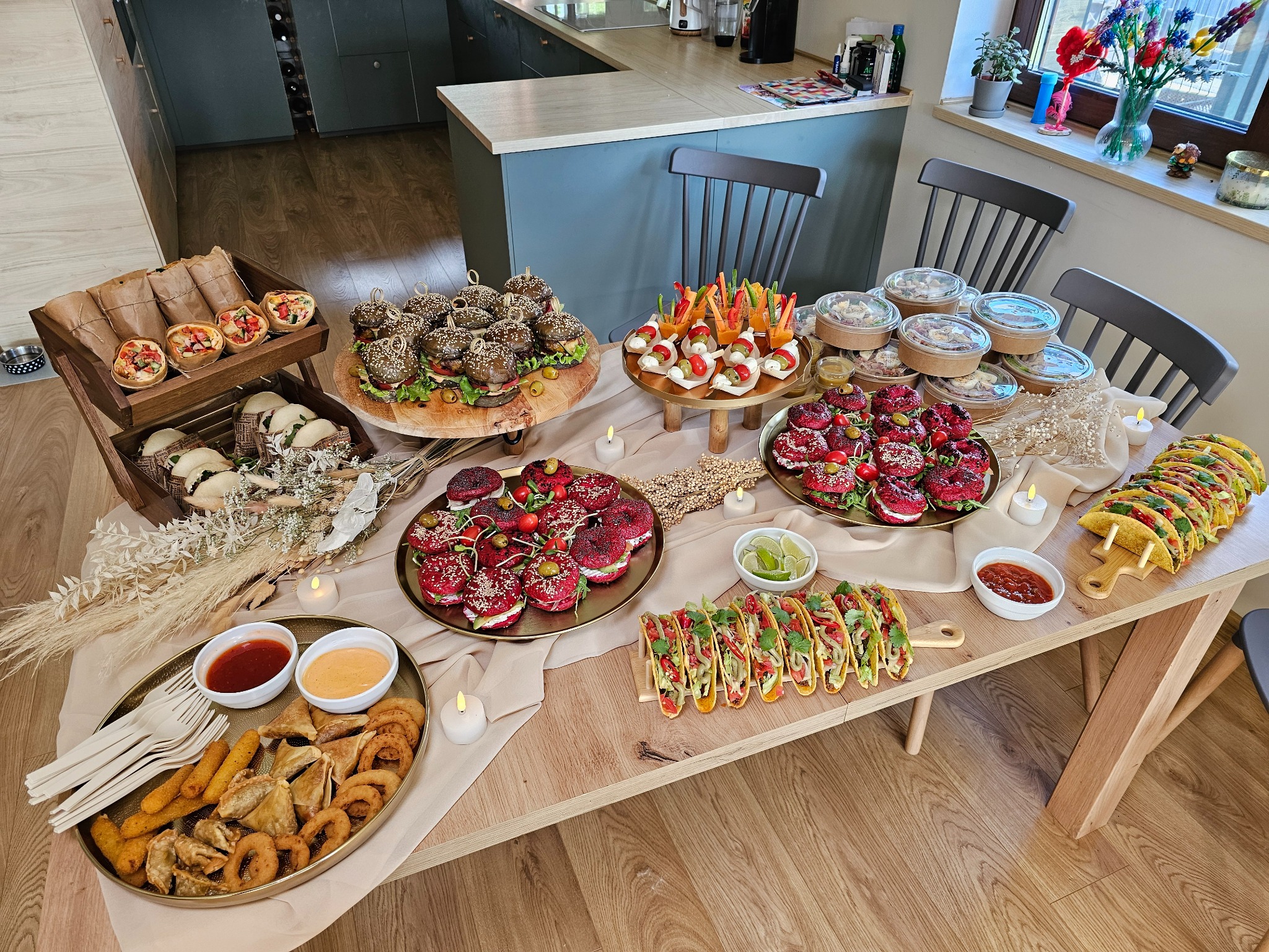 Stół z różnorodnym, estetycznie podanym cateringiem: burgery, przekąski warzywne, tacos, pierożki, sosy i świeczki. Idealne na imprezę firmową lub świąteczną.