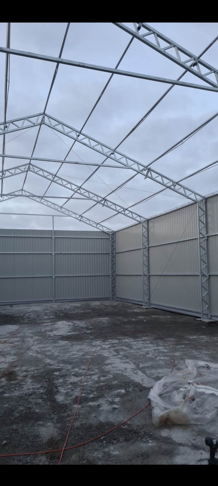 Konstrukcja metalowa hali magazynowej w trakcie budowy, widok od wewnątrz na szkielet i ściany z blachy trapezowej, pochmurne niebo w tle.