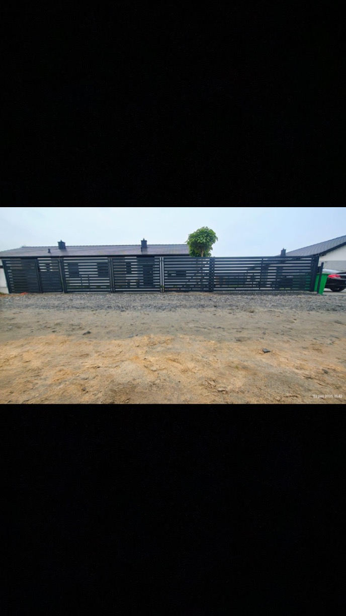 Nowoczesna, pozioma brama wjazdowa z metalowymi panelami w kolorze antracytowym, zintegrowana z ogrodzeniem. Widok z zewnątrz, na tle domu z ciemnym dachem.