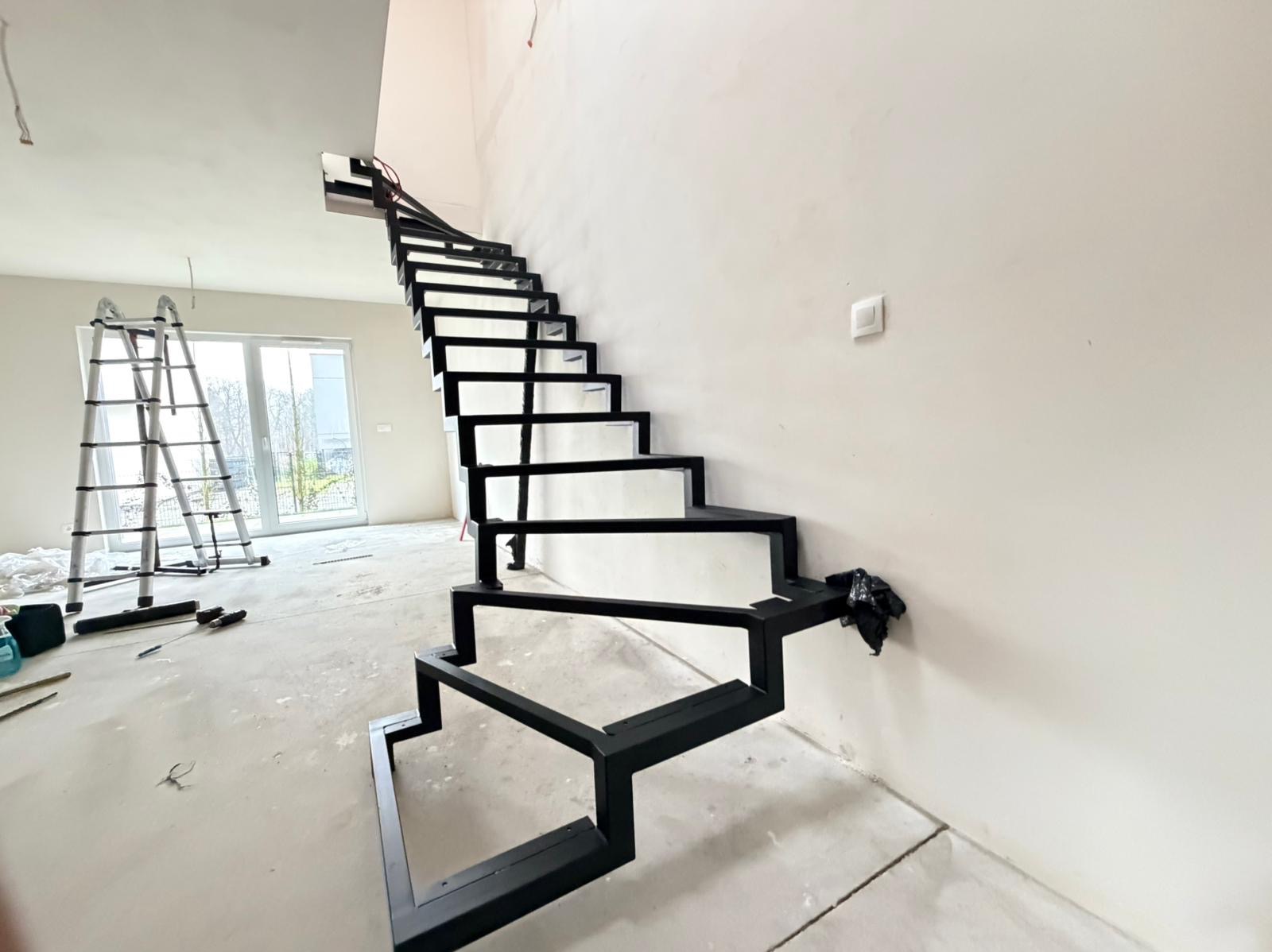 Nowoczesne, czarne schody metalowe o geometrycznym designie w surowym wnętrzu. Widoczna drabina i przygotowania do wykończenia podłogi.