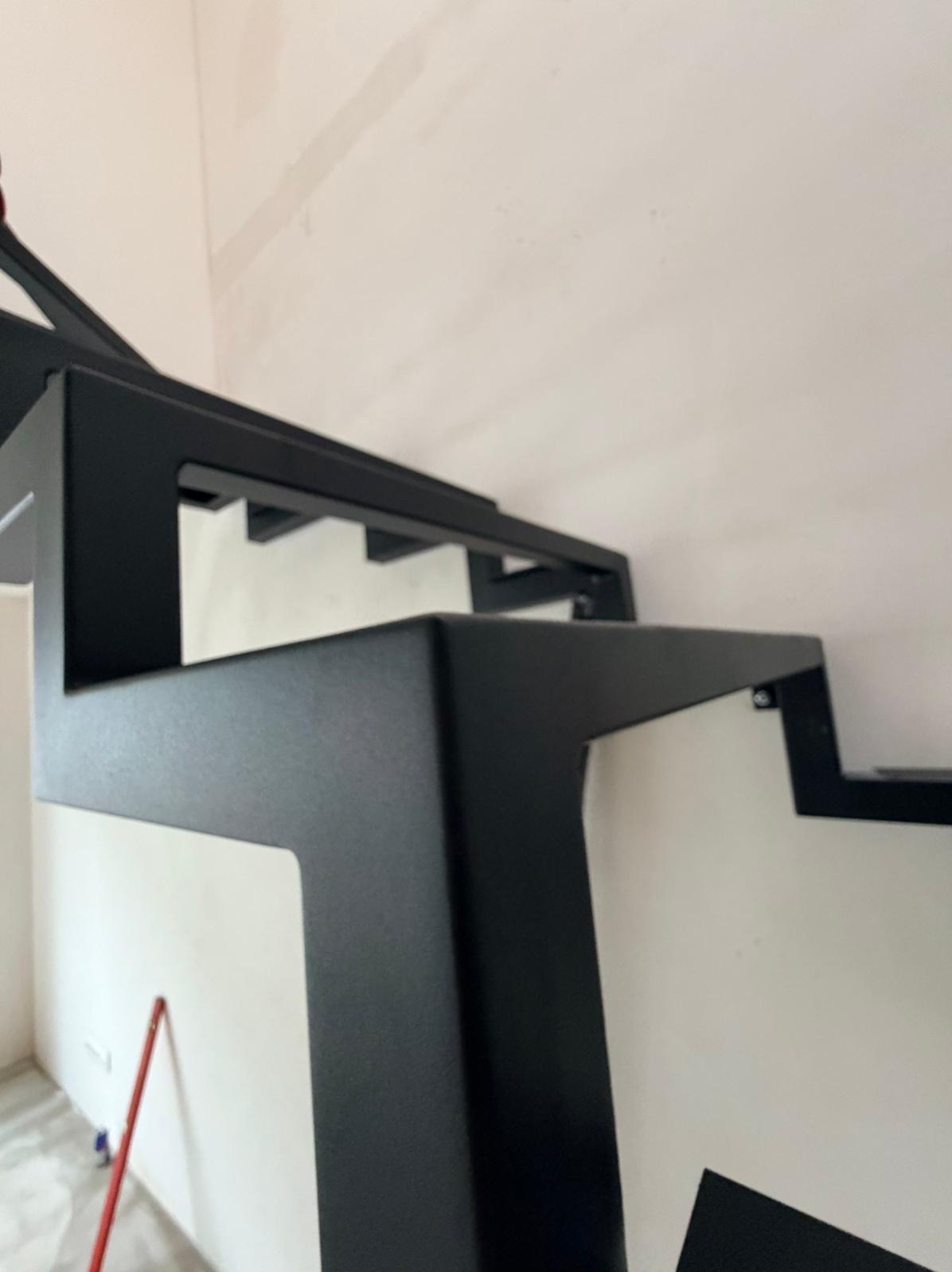 Nowoczesne schody metalowe w kolorze czarnym, z geometrycznymi elementami konstrukcyjnymi, widoczne z bliskiej perspektywy, w trakcie montażu w jasnym wnętrzu.