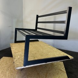 ArtLoftHome - Metalowy stelaż sofy w stylu industrialnym, czarne profile na tle surowej płyty OSB. Minimalistyczny design, spawane łączenia, widoczne niedoskonałości powierzchni.