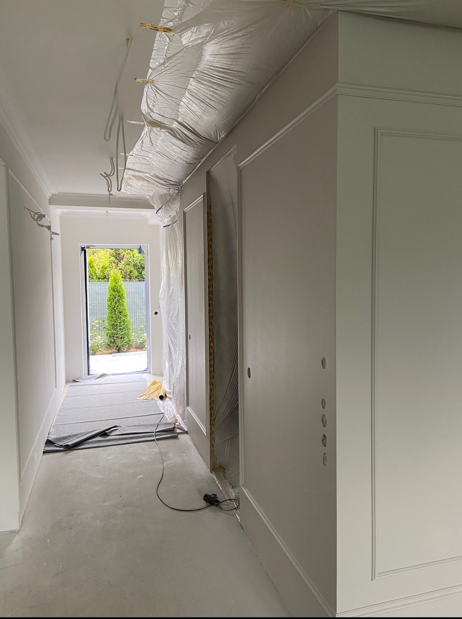 Korytarz w trakcie prac wykończeniowych: zabezpieczone elementy, świeżo pomalowane ściany z dekoracyjnymi listwami i otwory na gniazdka elektryczne.
