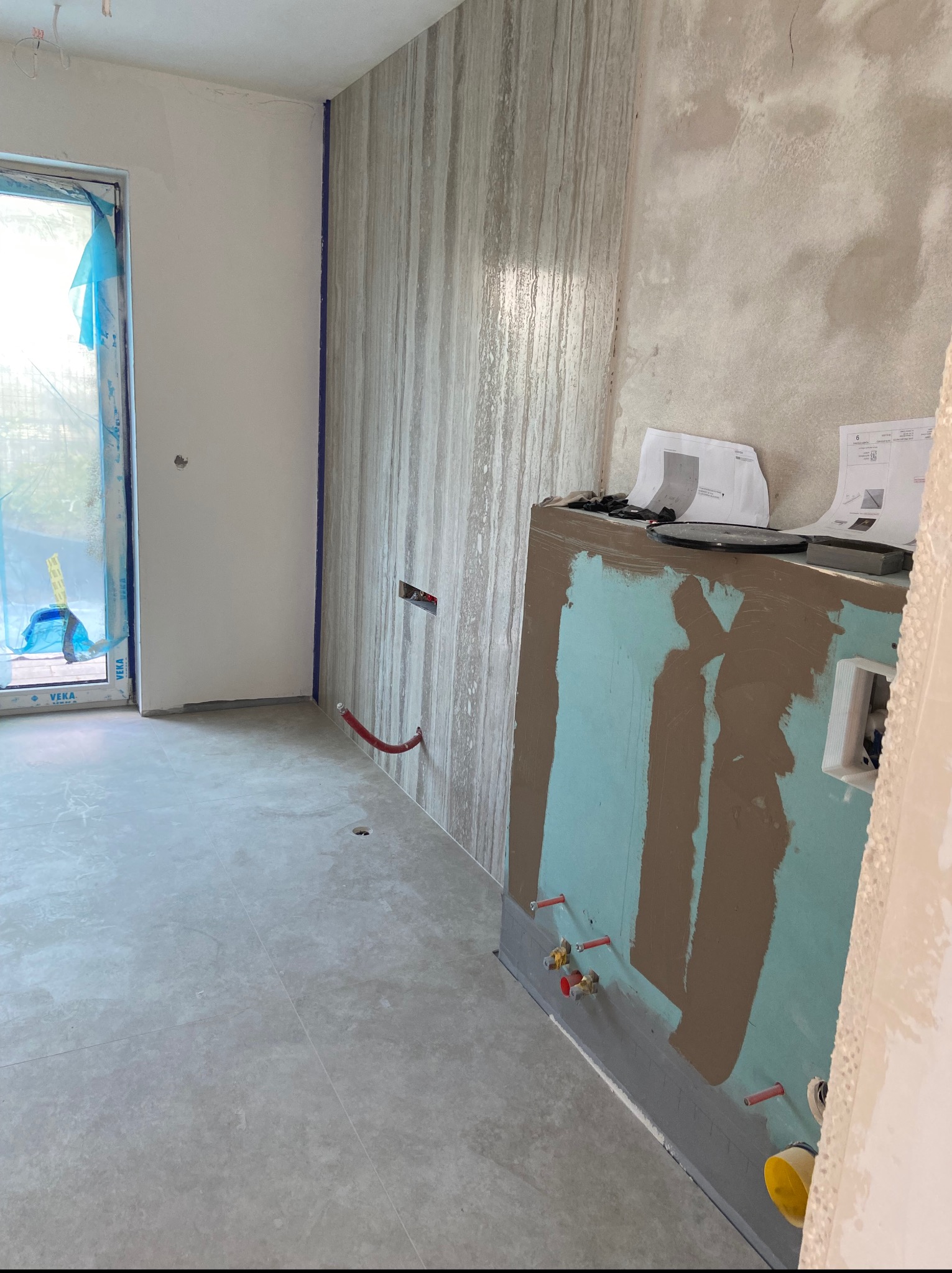 Wnętrze łazienki w trakcie remontu: częściowo wyłożona ściana płytkami imitującymi drewno, przygotowana pod zabudowę stelaża WC z instalacją wodną.